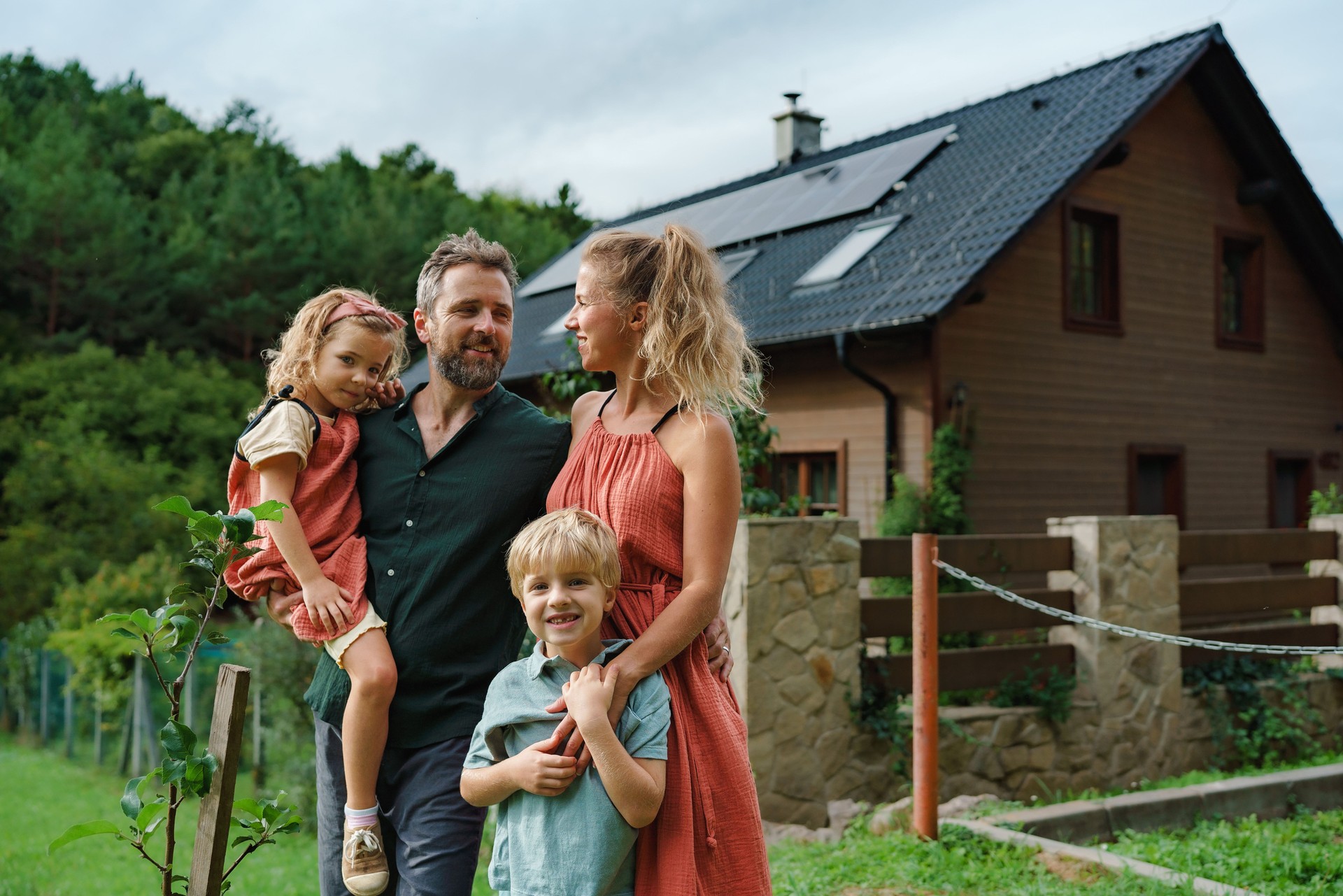 Familia feliz cerca de su casa con paneles solares. Energía alternativa, ahorro de recursos y concepto de estilo de vida sostenible.